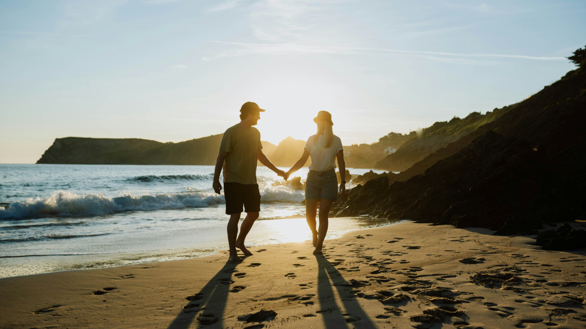 A young couple walk on a sandy beach at sunset