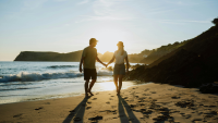 A young couple walk on a sandy beach at sunset