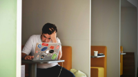 A man works at his laptop in a shared working area. He looks stressed.