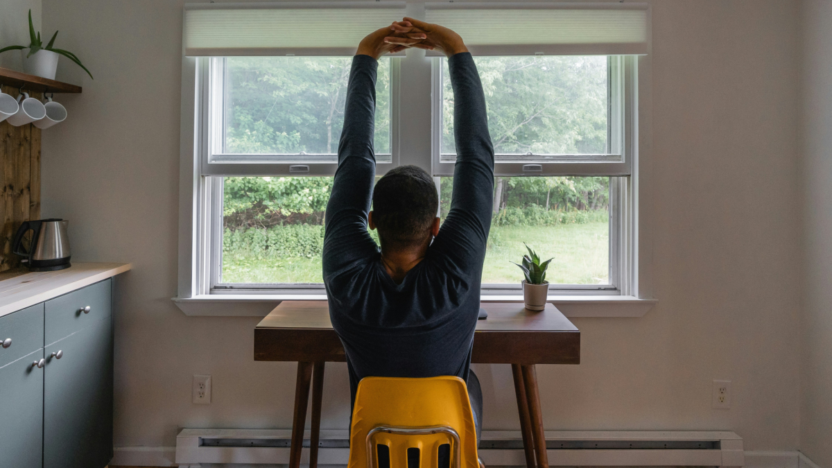 A man looks out over his garden and stretches as he works at his desk
