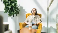 A woman sits in a chair with her eyes closes and listens to her headphones