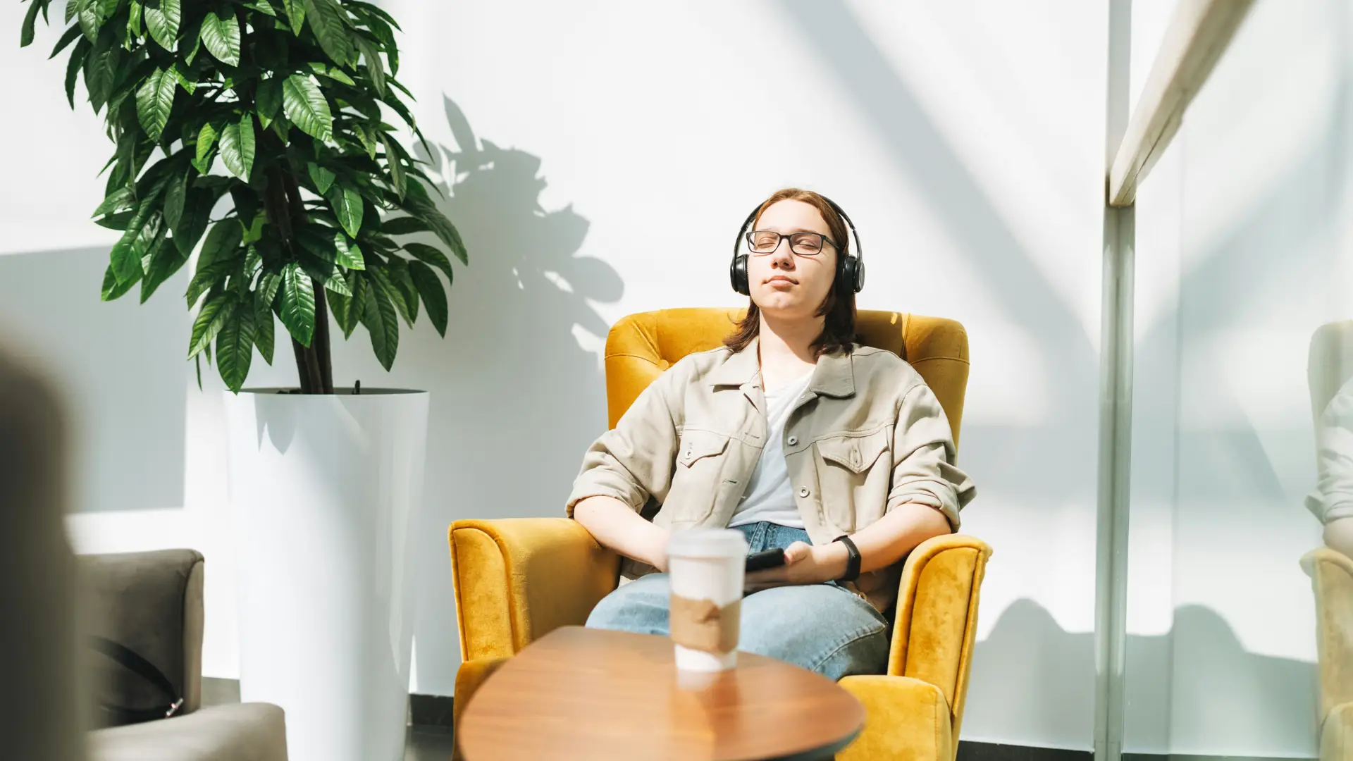 A woman sits in a chair with her eyes closes and listens to her headphones