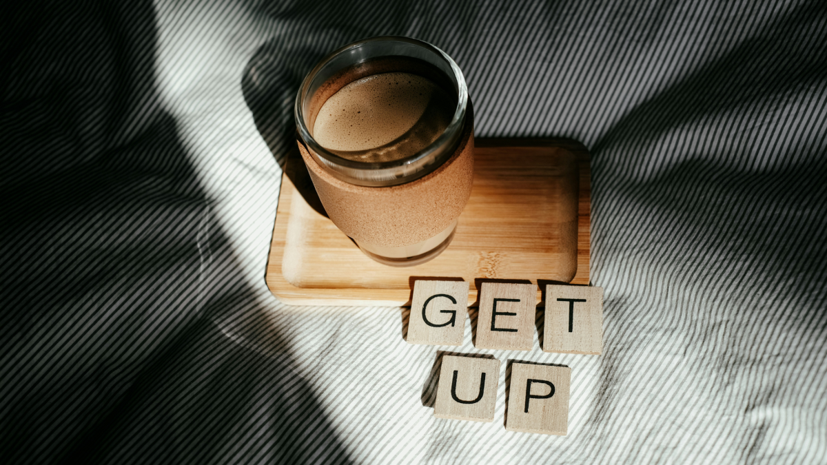 A picture of a coffee on a bed with a message that says 'get up'