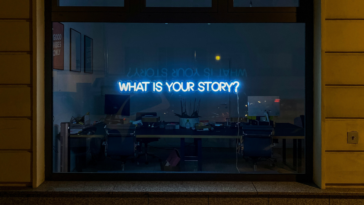 An image of a window with 'what's your story?' written in neon