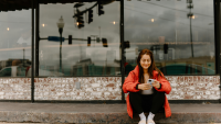 a woman sits on a curb and smiles at her phone