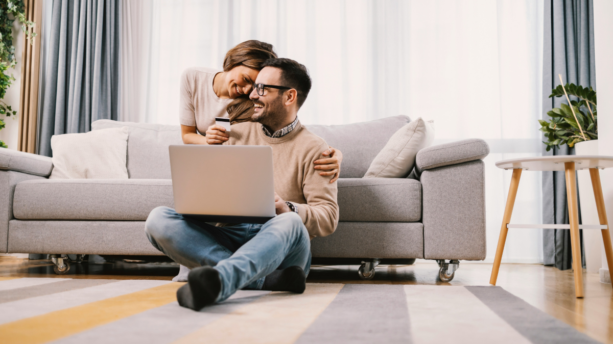 a woman hugs a man from behind while she sits on a couch