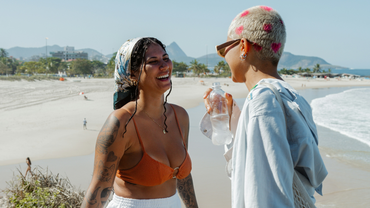 two young woman laugh and chat on a beach