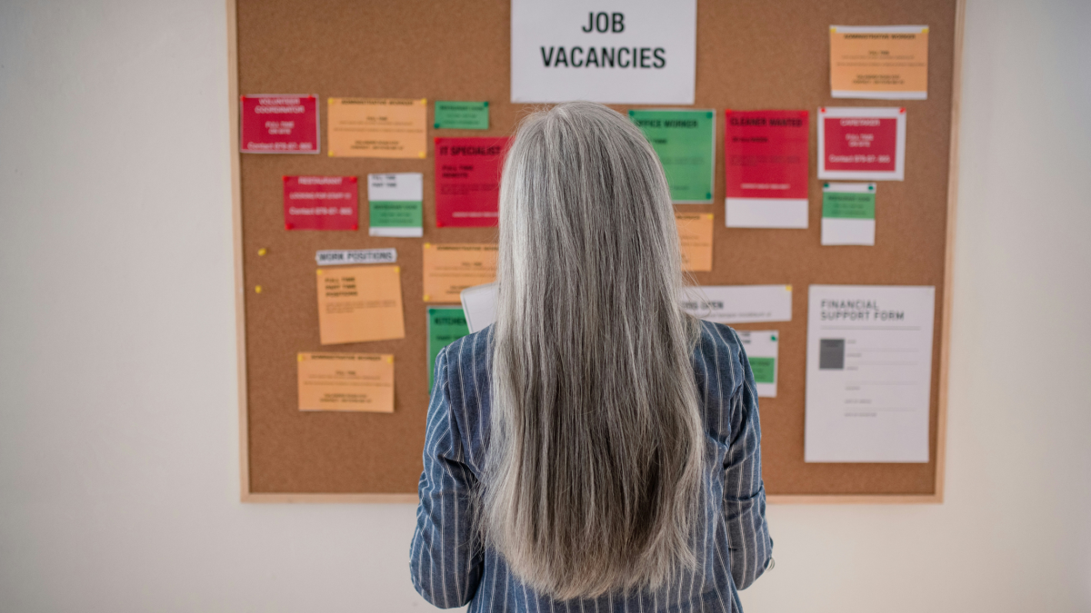 a grey haired woman looks at a job vacancy board