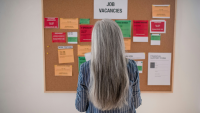 a grey haired woman looks at a job vacancy board