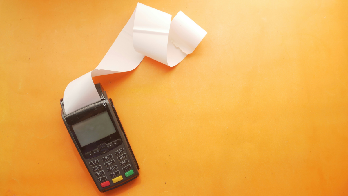 a card machine with a long, blank receipt against an orange background