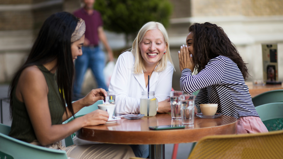 Young women are talking and laughing at a table, sharing secret