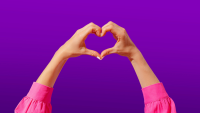 A lady makes a heart with her fingers against a purple background