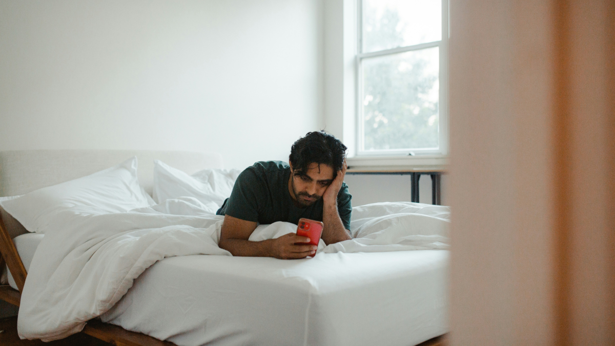 a man lies on his bed looking at his phone