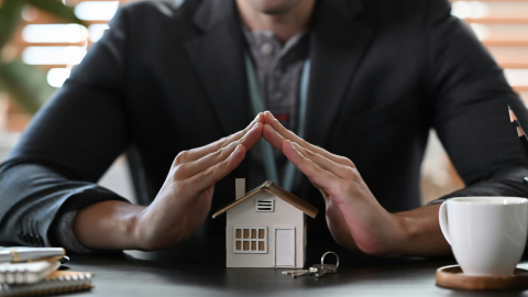 a man arcs his hands over a small, model house