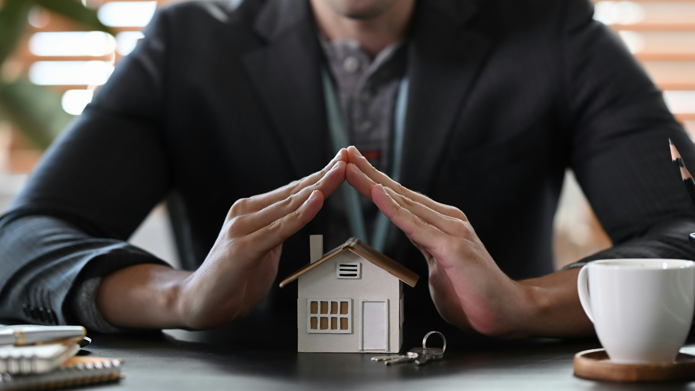 a man arcs his hands over a small, model house