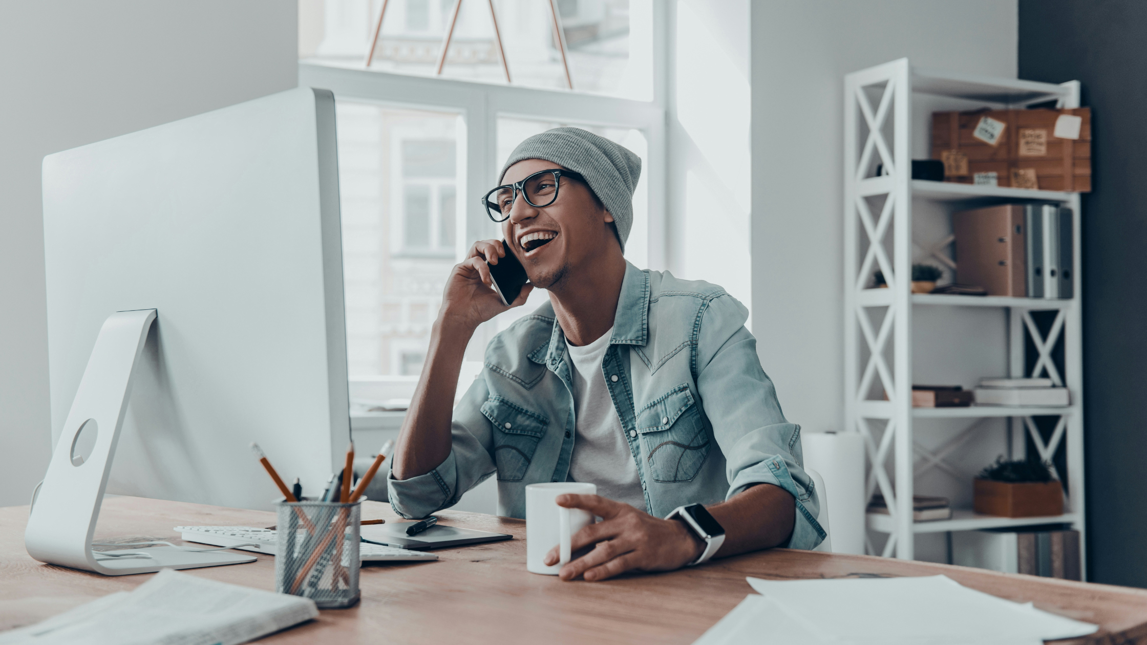 a man sits at his desk and laughs while on his phone
