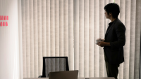 An office worker looks out of his window through the blinds.