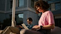 A woman and a man sit together and smile at their laptops
