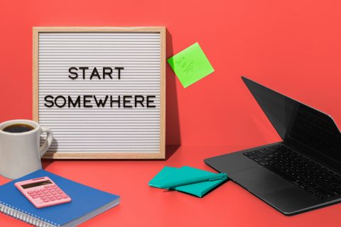 A board next to a laptop says the words 'start somewhere'