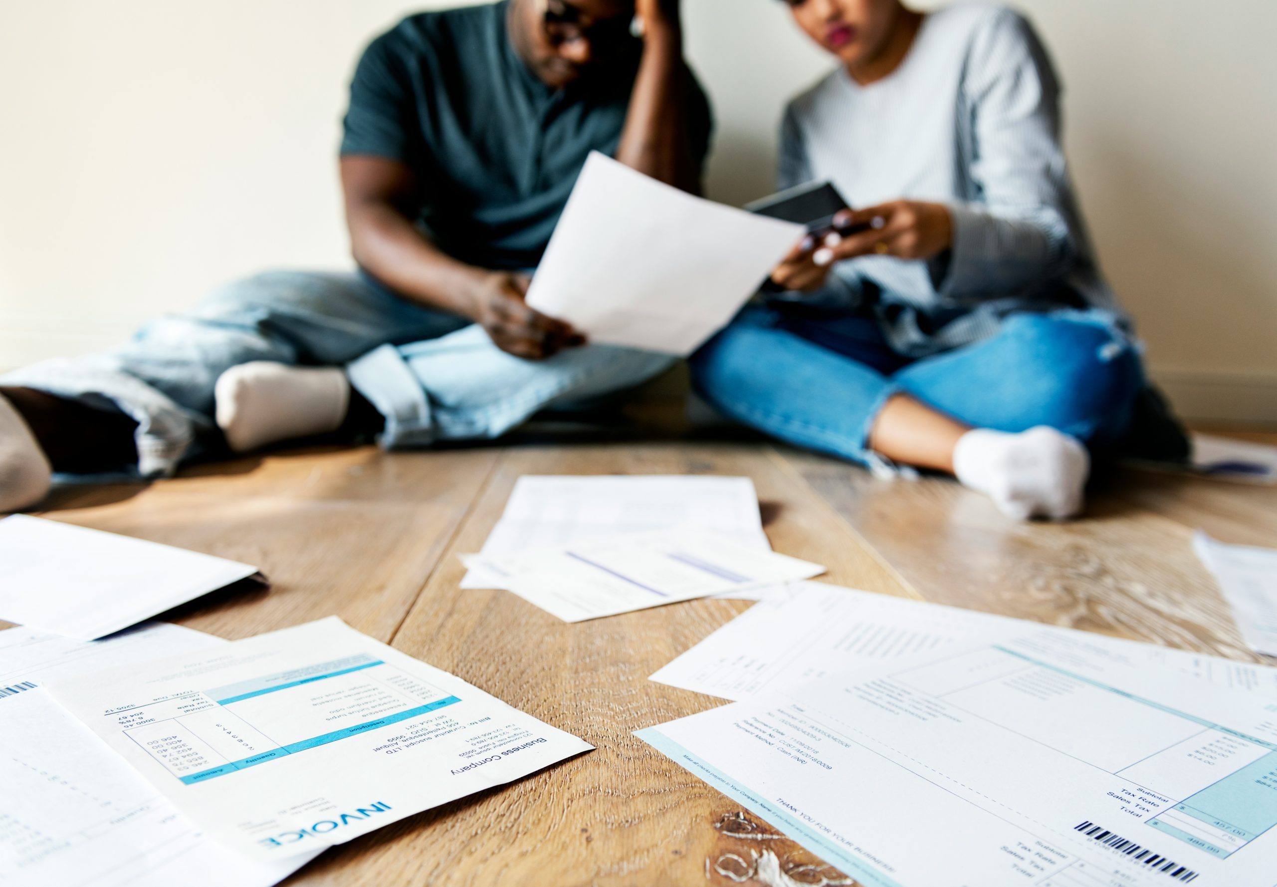 A young couple sit on the floor, surrounded by documents, looking worried