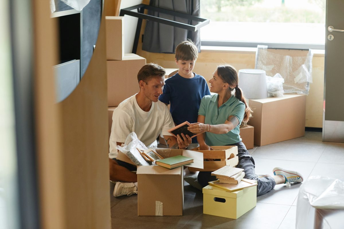 A young family sit surrounded by moving boxes