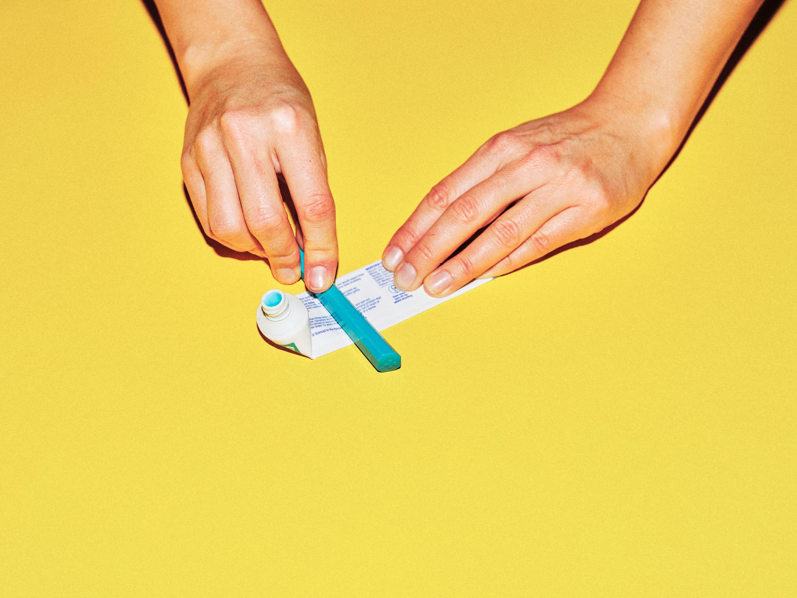 Someone squeezing the last bit of toothpaste out of a toothpaste tube.